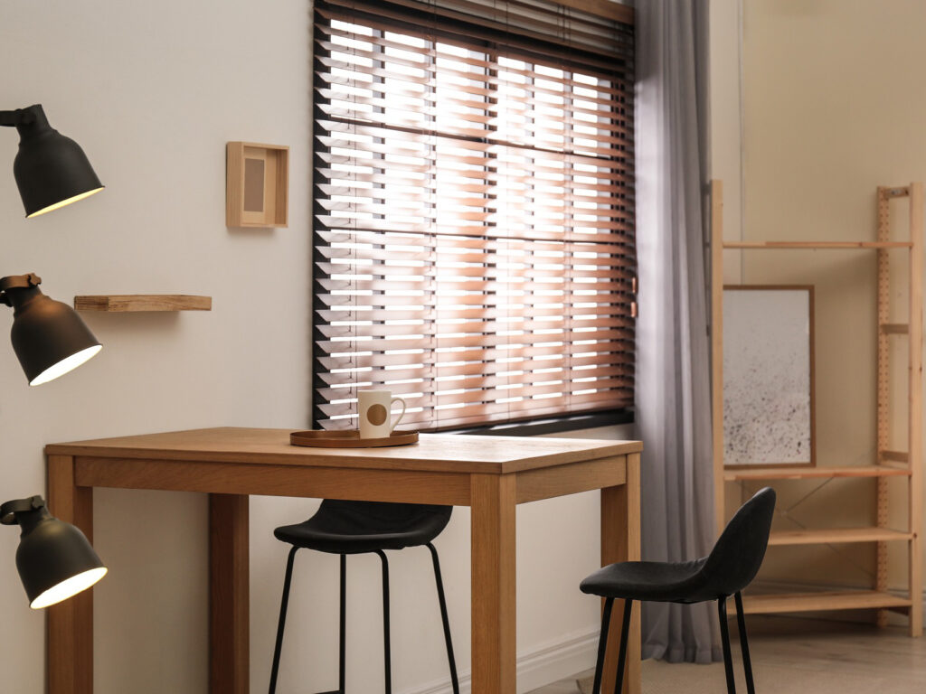 A living space with table and chairs and the sun shining through the window blinds