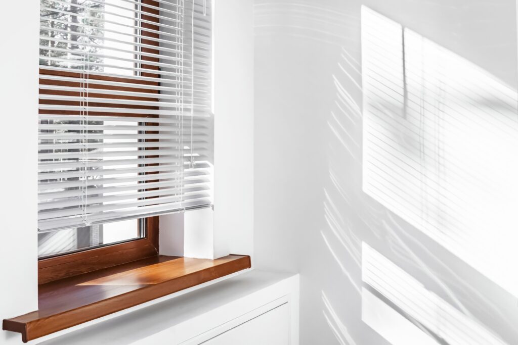Corner of room with white wall, and window with white Aluminium Venetian Blinds.