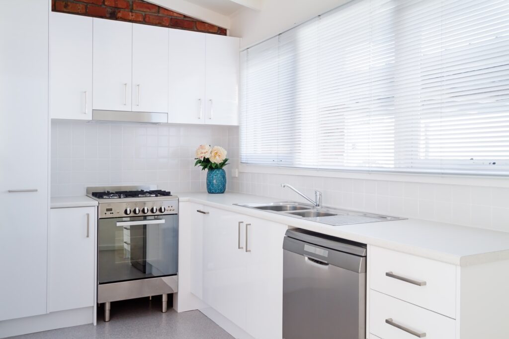 Image alt tag: Bright kitchen with white cabinets, stainless steel appliances, and Fauxwood Venetian Blinds.
