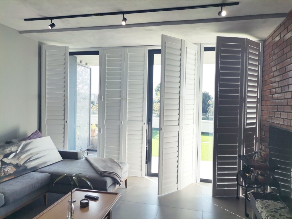 Lounge with dark grey couch, and semi open white Aluminium Shutters.