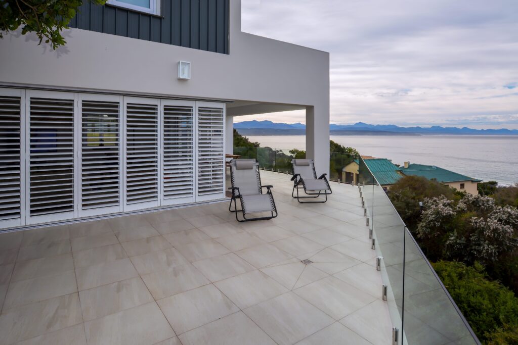 Outside view of coastal home with ocean views, white loungers, and white security shutters.