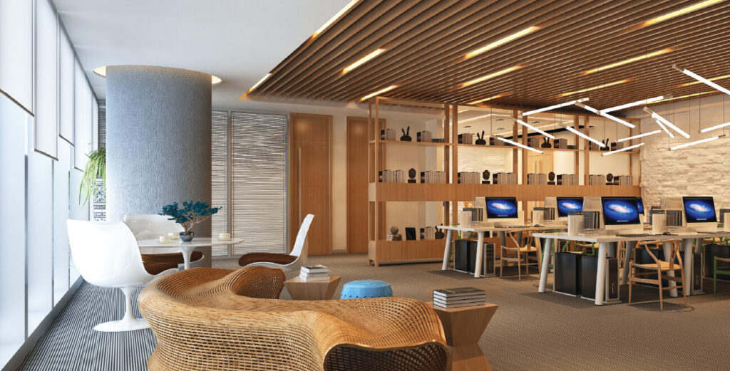 Open office space with a lounging area, wooden desks with computers & shelves, with light filtering roller blinds covering the windows.